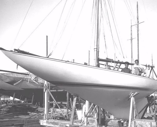 Black and white photograph of a boat on land propped up in a boatyard
