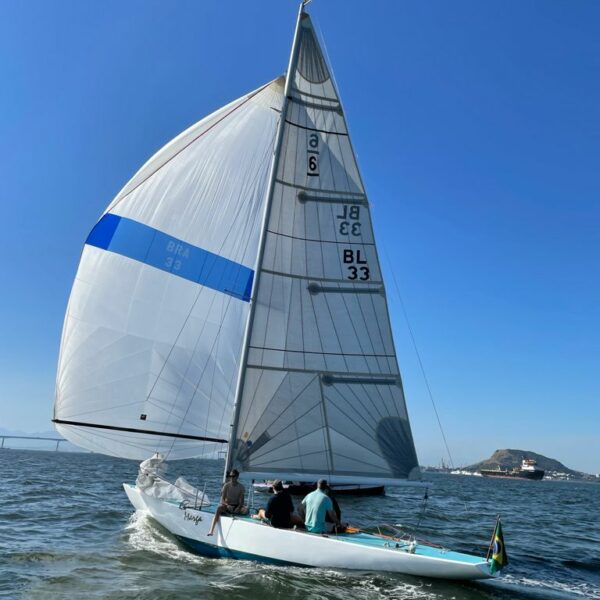 Six Metre sailing on the ocean with mountains in the background while Brazilian flag waves with the wind.