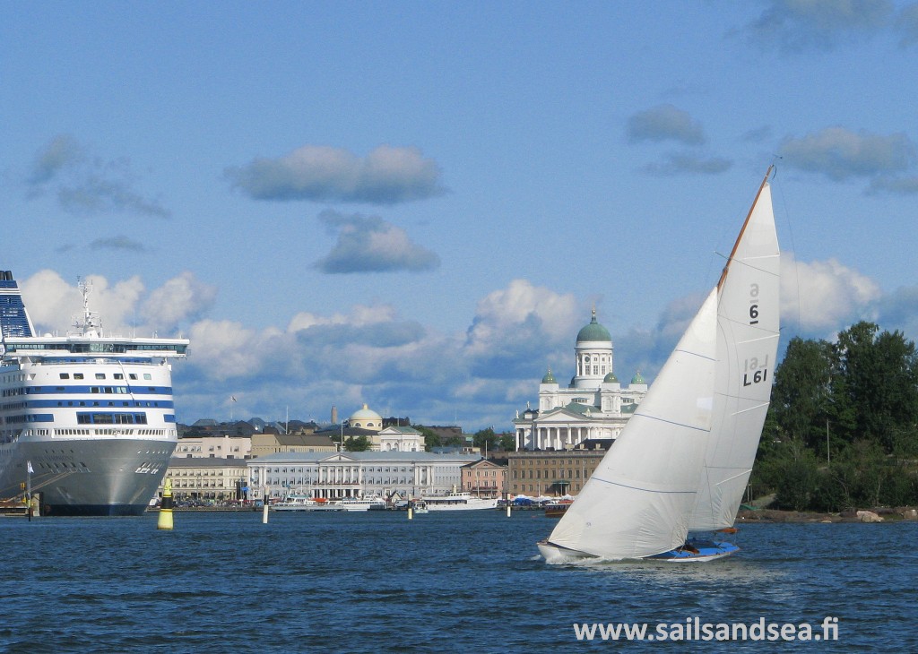 Sailing boat underway with buildings and cruise ship inthe background