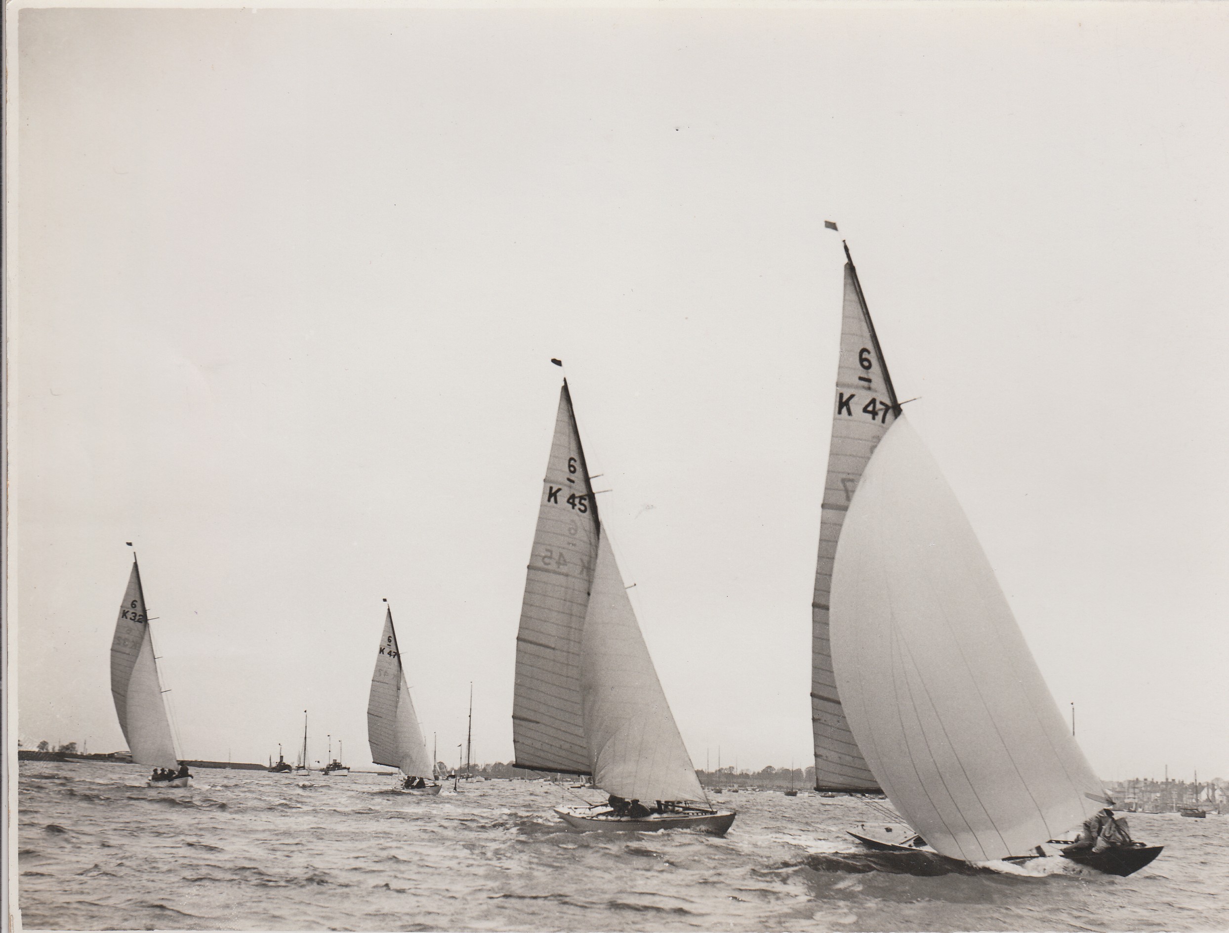 Black and white photograph of four Six Metre sailing boats racing.