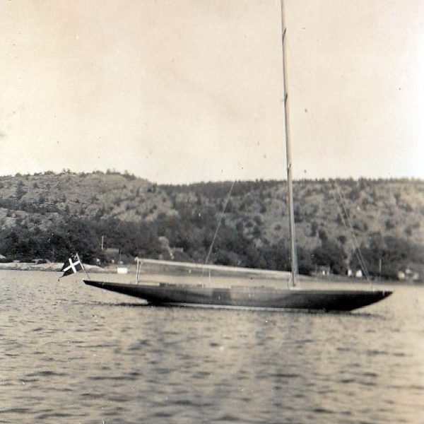 Black and white photograph of a moored Six Metre sailing boat. She is flying a Danish ensign flag.