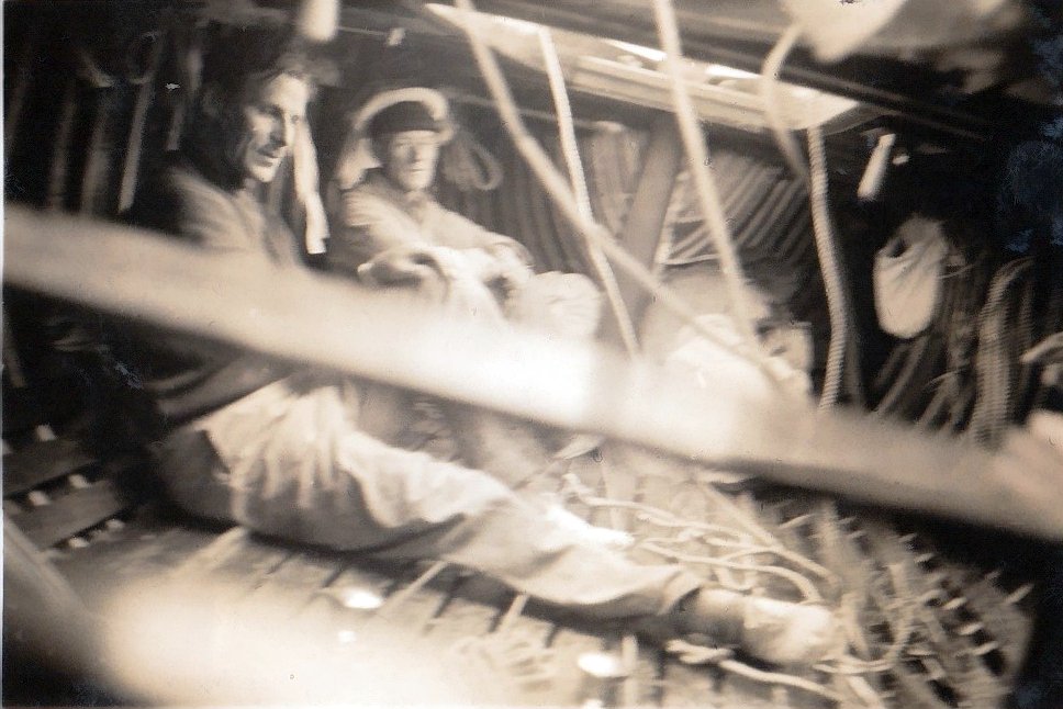 Black and white photograph taken below deck on a Six Metre sailing boat. Two crew members are seated on the floor of the boat.