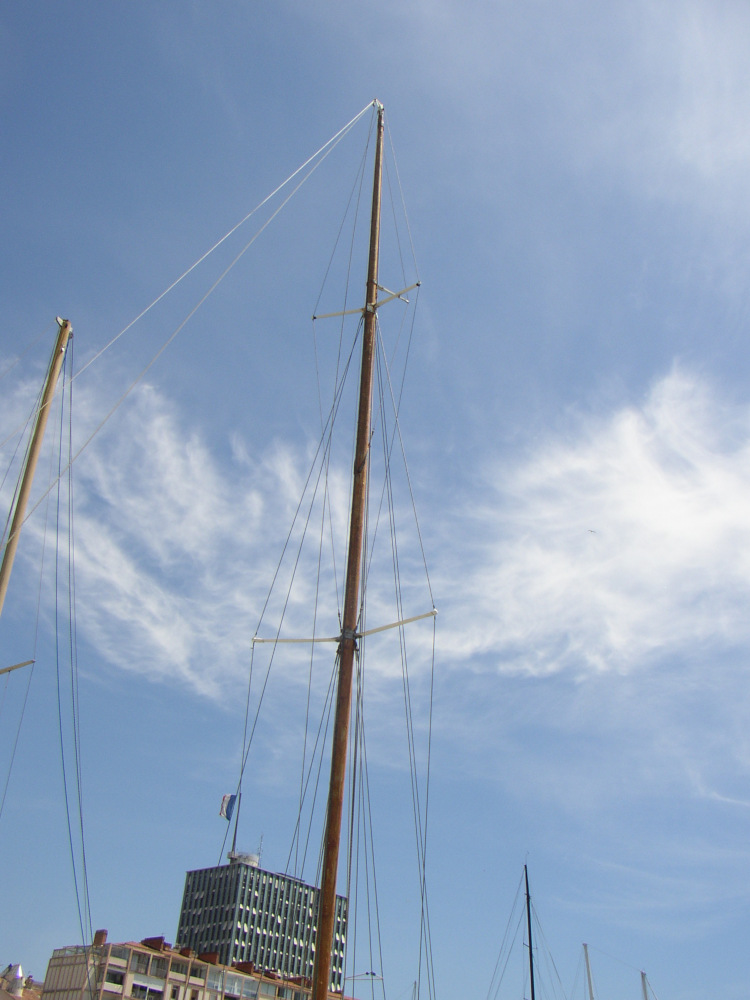 Mast of a yacht moored under a blue sky. The sail is down.