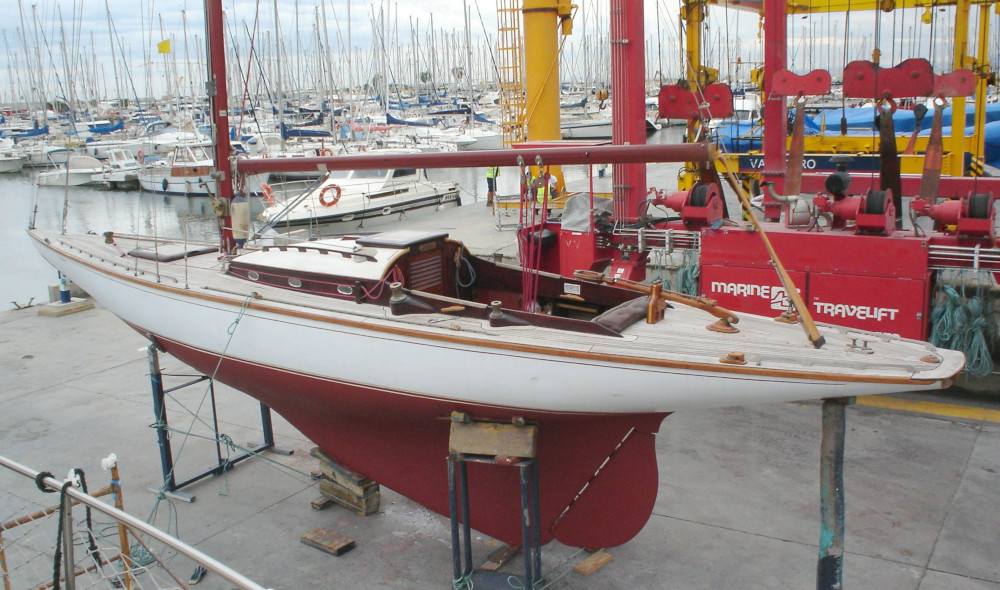 A colour photo of a red and white yacht on the hard