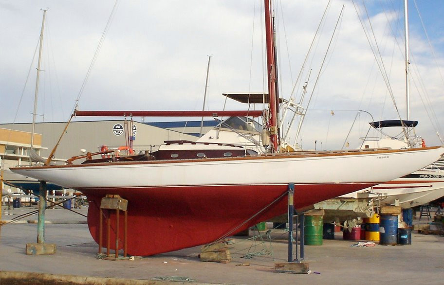 A colour photo of a red and white yacht on the hard