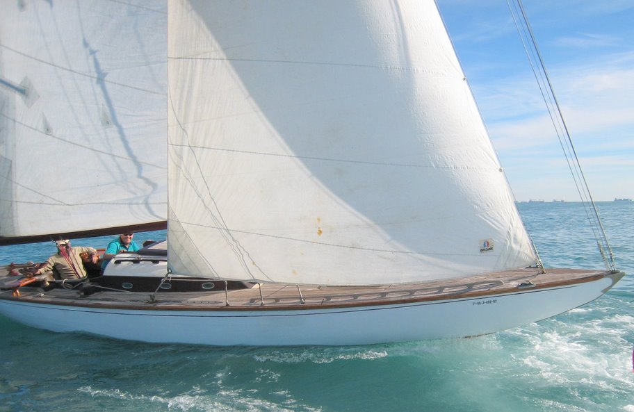 A colour photo of a wooden yacht sailing in blue waters