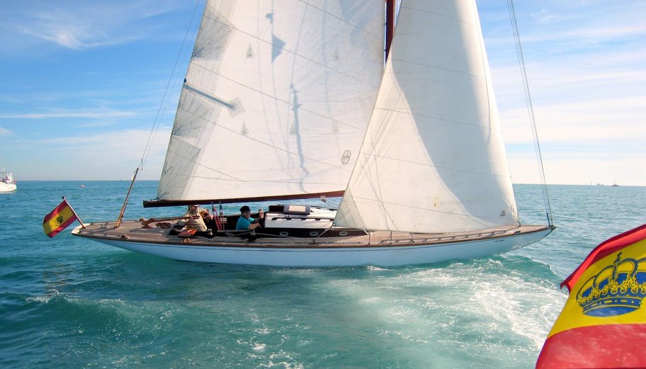 A colour photo of a wooden yacht sailing in blue waters