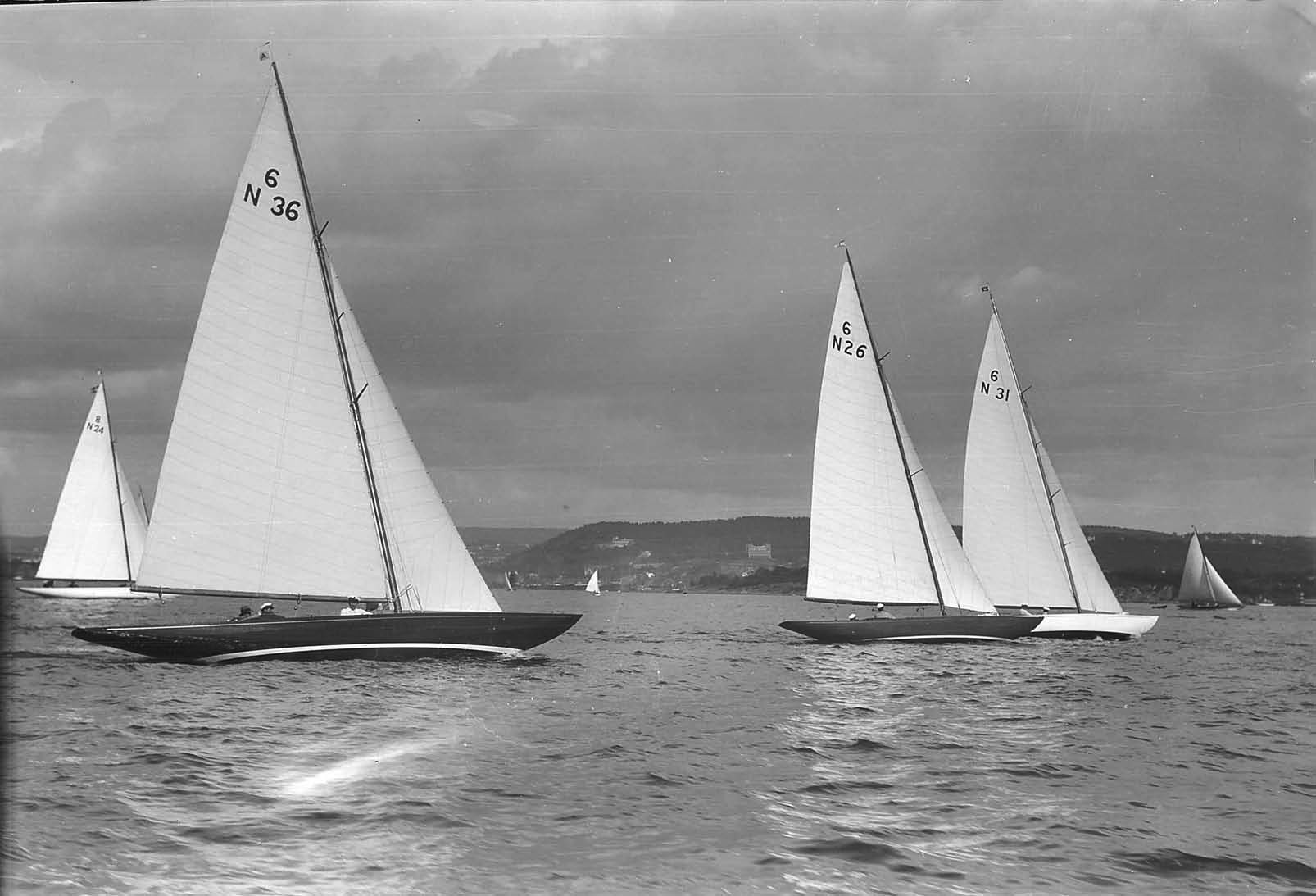 Black and white photo of a group of yachts with white sails sailing