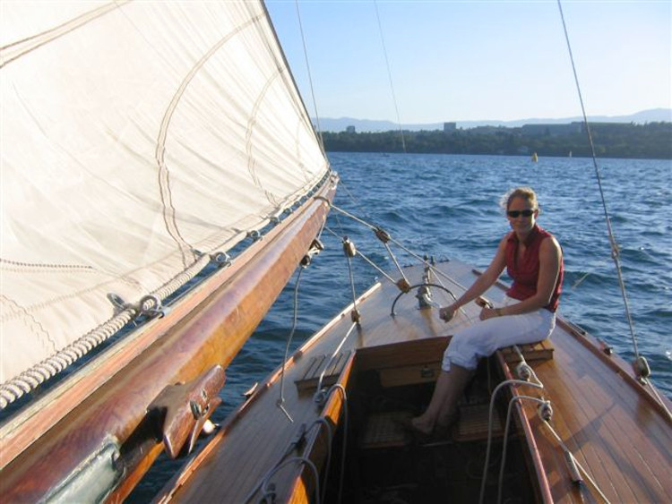 Colour photo of a yacht sailing. A crew member sits on the deck