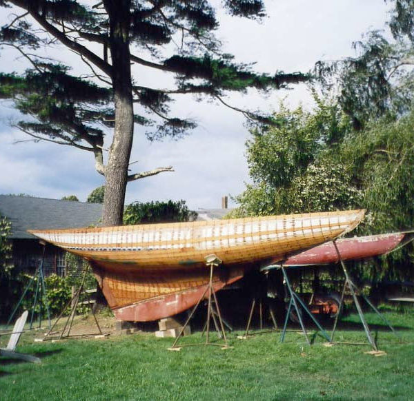 A bare wooden yacht hull on supports on grass