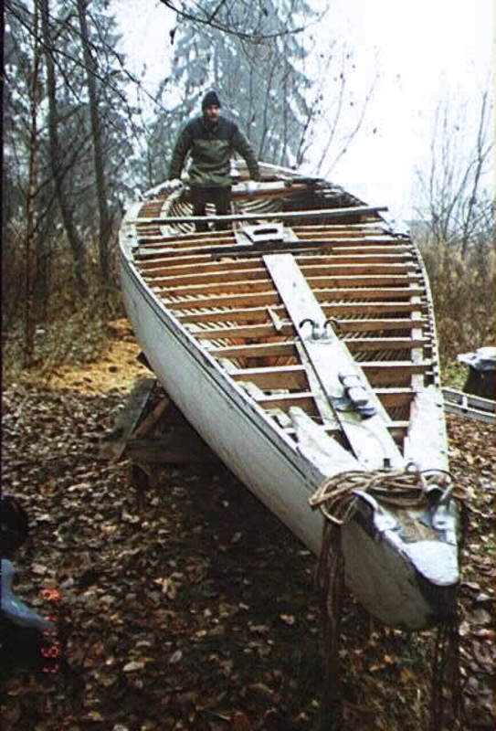Colour photo of a yacht hull in poor condition stored outside near woodland