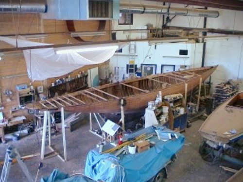 A wooden hull of a yacht inside a workshop.