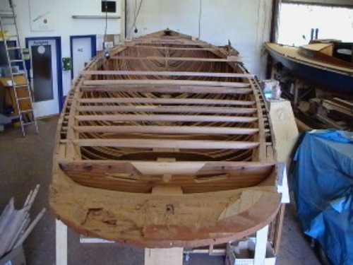 A wooden hull of a yacht inside a workshop.