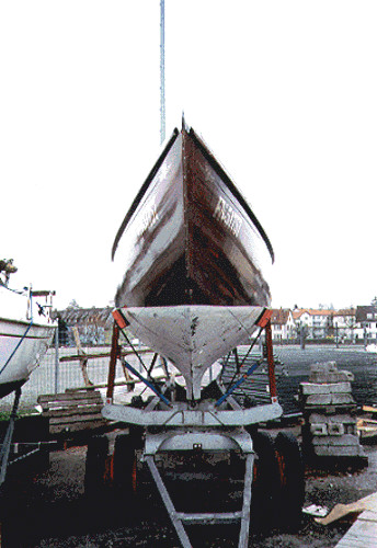 A treated wood yacht hull with a white keel on a white trailer.