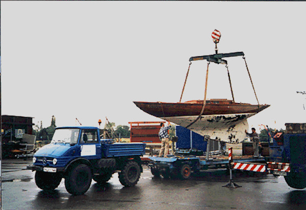 A treated wooden yacht hull with a white keel being hoisted onto or off a blue trailer