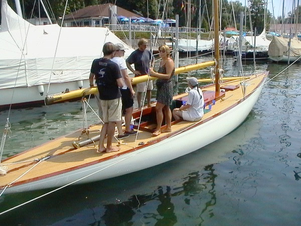 A white yacht with a wooden deck in blue water with 5 people on the deck.