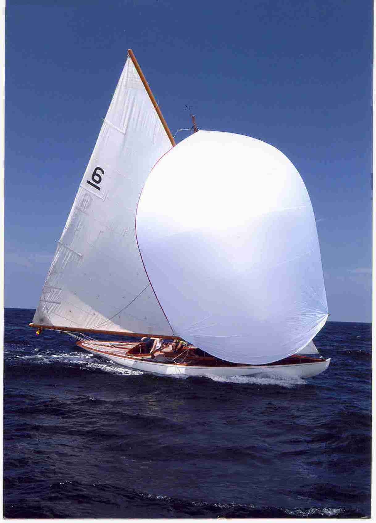 White yacht with a white sail and spinnaker. The sky and water is blue.