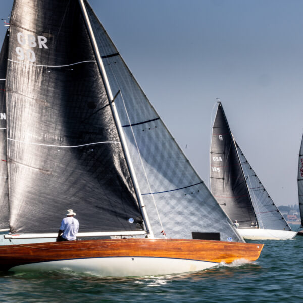 Six Metre boats sailing on water under blue sky with crew members visible